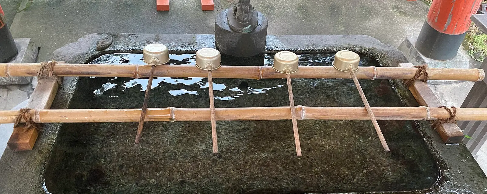Metal ladles resting on a stone purification basin with a dragon spout at a shrine