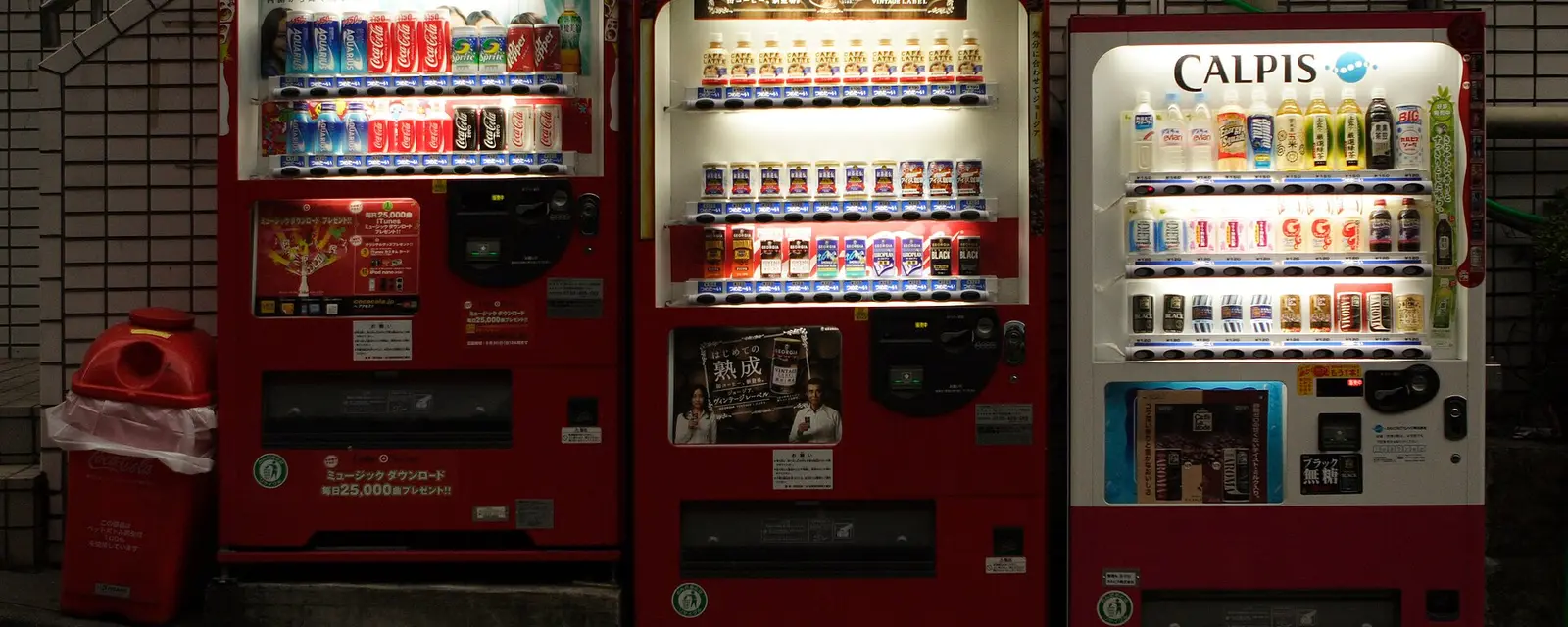 Three brightly lit Japanese drink vending machines on a night street